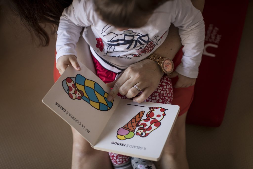 Bambina legge un libro illustrato con l'aiuto di un adulto.