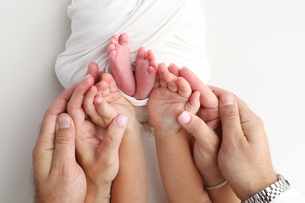 Mani di diverse età toccano i piedini di un neonato
