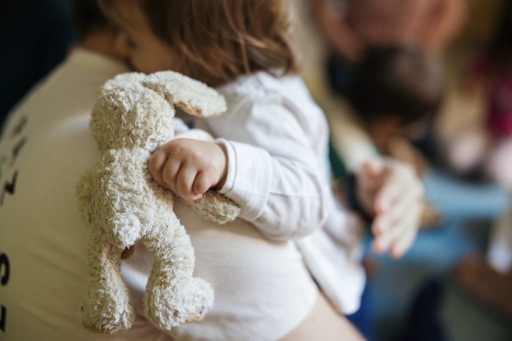 Bambina in braccio a un adulto tiene in mano un peluche