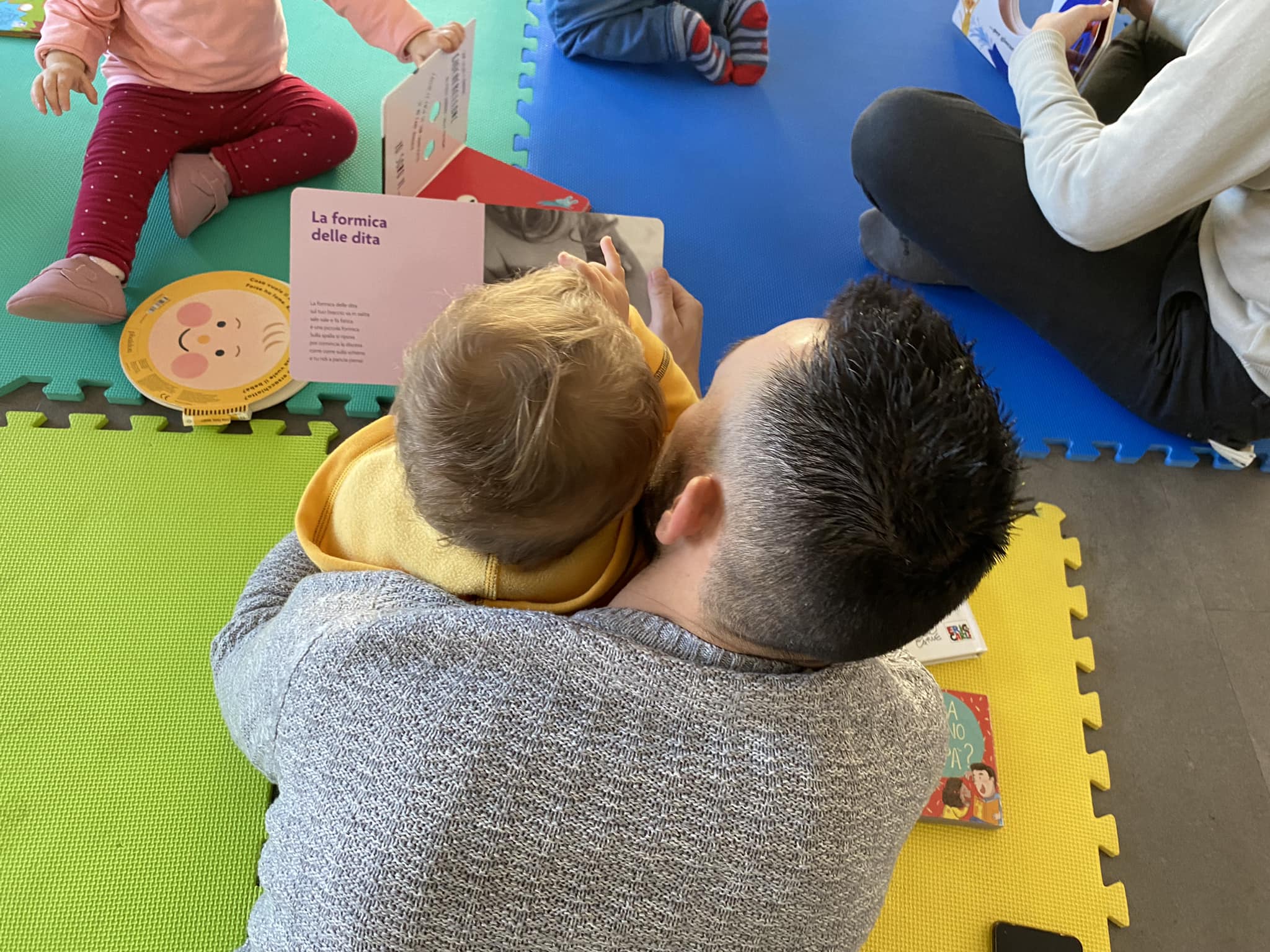 Papà e figlio leggono insieme sul tappetone del nido