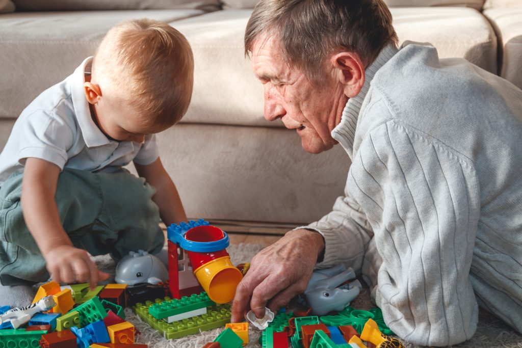 Un nonno e un bambino costruiscono insieme con i mattoncini colorati, seduti a terra in salotto