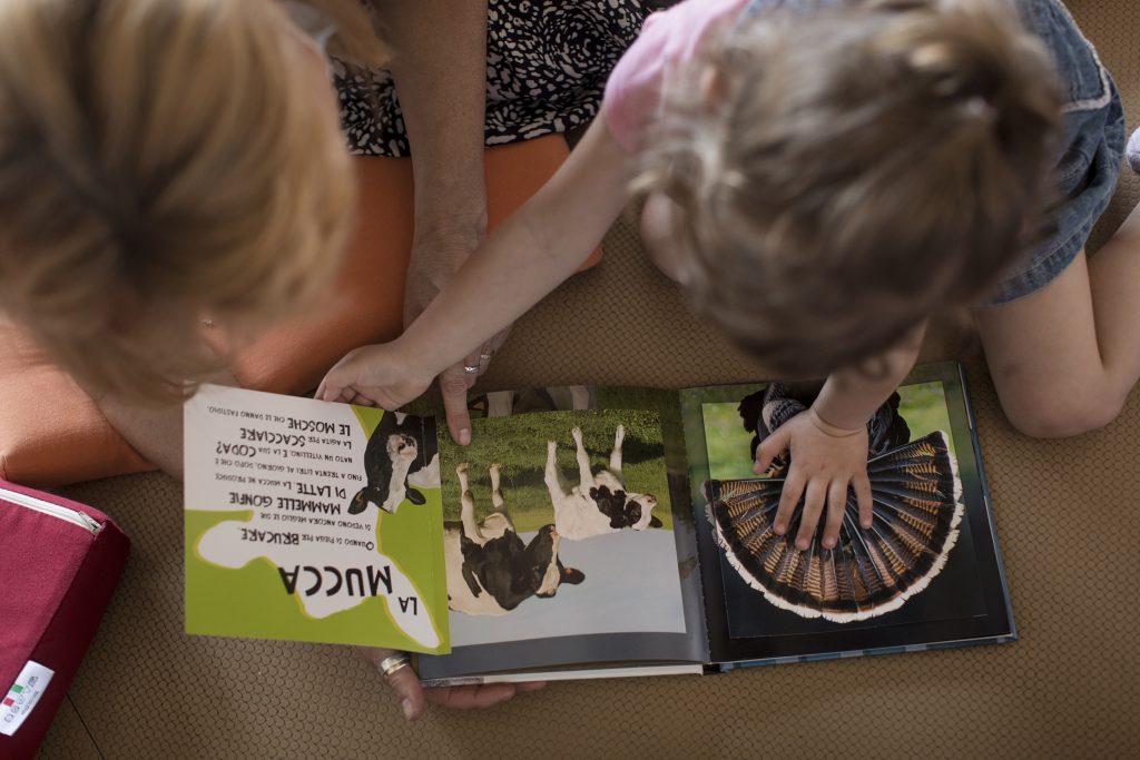 Una bambina indica le fotografie di un libro sugli animali mentre un’adulta sfoglia le pagine con lei
