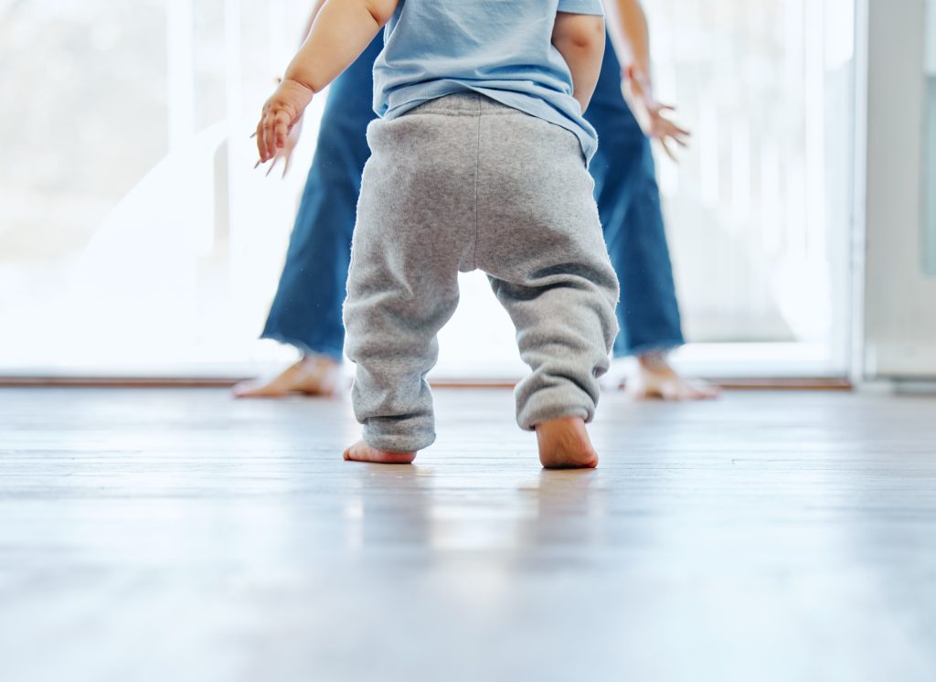 Un bambino muove i primi passi a piedi nudi verso una persona adulta.
