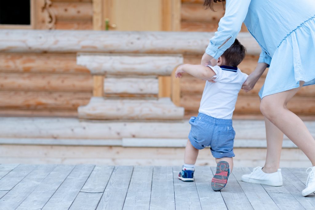 Una persona adulta sorregge un bambino mentre muove i primi passi all'aperto.